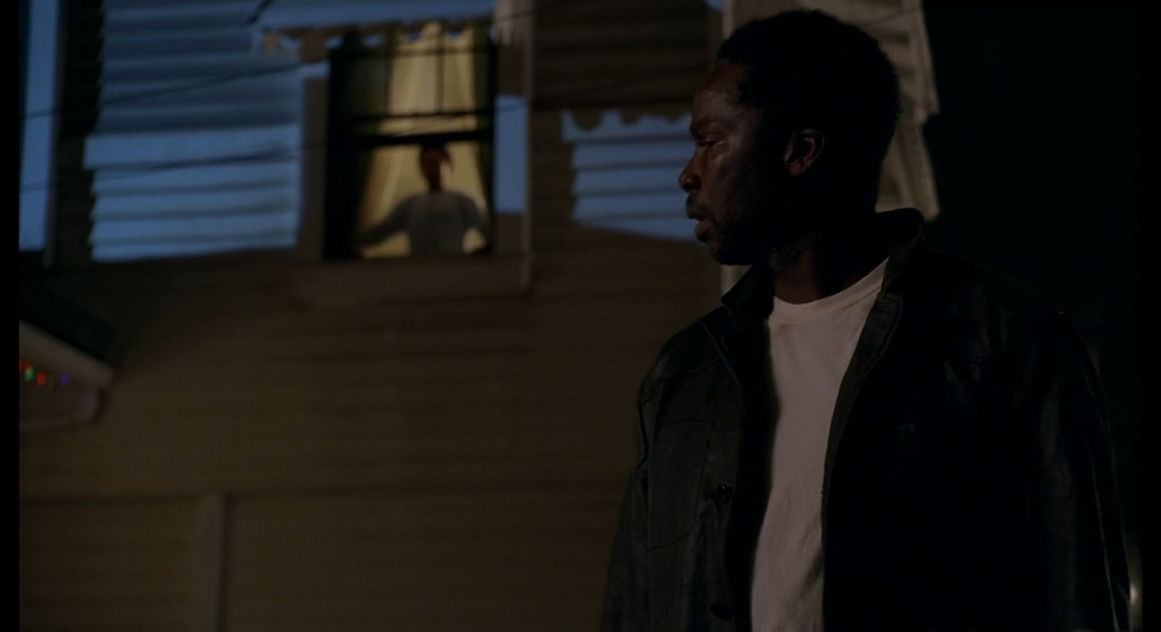 Michal, standing outside a house, looks over his shoulder at Walt in an upper story window.