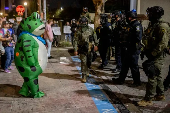 A protester in a frog costume in front of federal officers Monday outside the ICE building in Portland