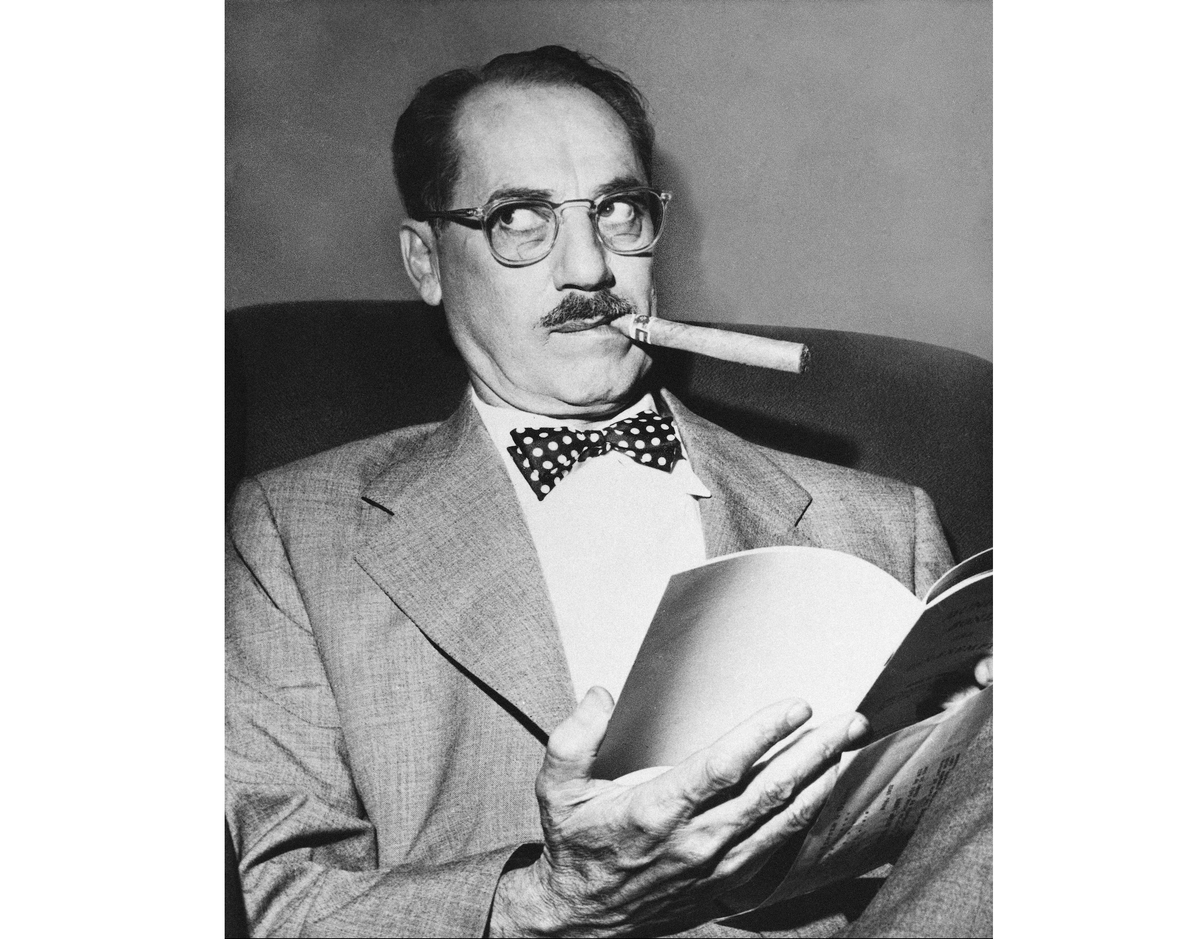 Groucho Marx reads a book and pulls a side-eye glance.