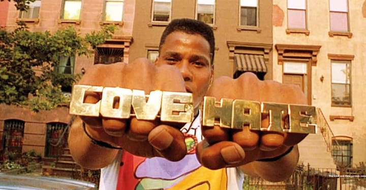 Radio Raheem (Bill Nunn) holds up brass knuckles. The right-hand says "LOVE," the left-hand says "HATE"