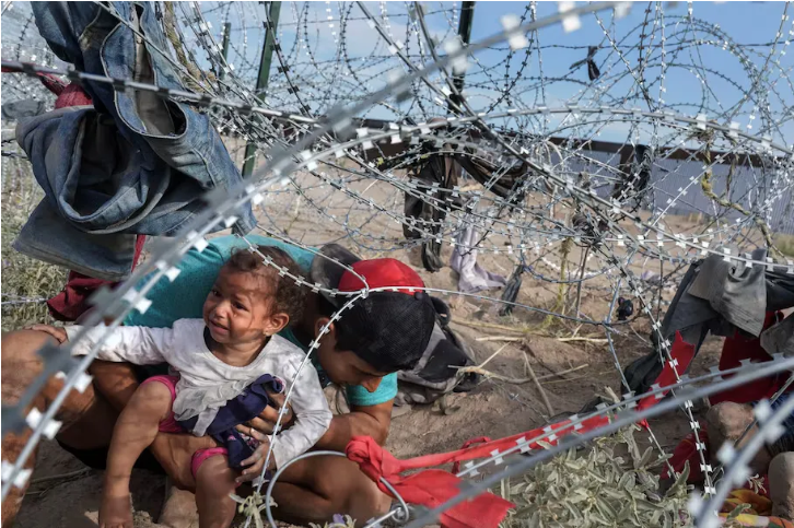 A man and a child move through tight coils of razor wire. (Michael Robinson Chávez/The Washington Post)
